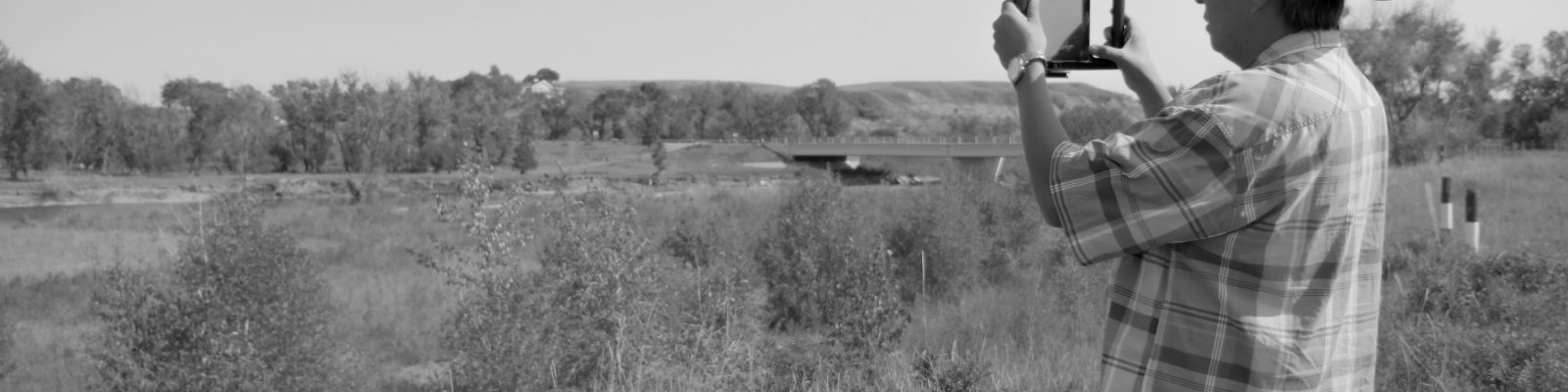 a man stands in a field holding a camera. the image is in black and white.