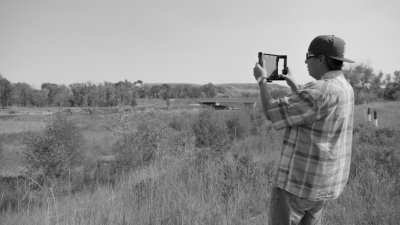 a man stands in a field holding a camera. the image is in black and white.